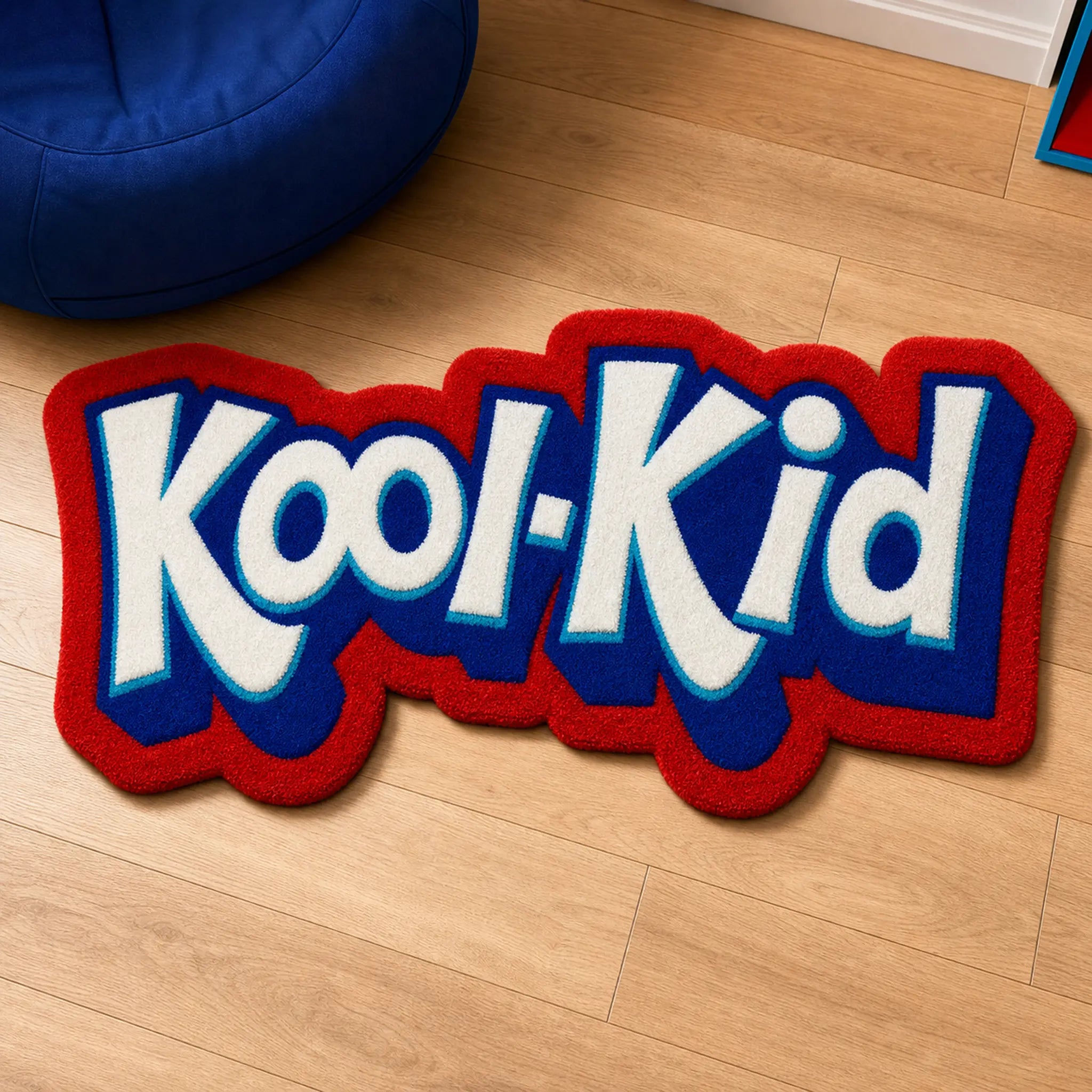 Kool-Kid Pop die-cut rug — cream bubble lettering on cobalt blue with a red outline, cut to the shape of the logo, on a wooden floor