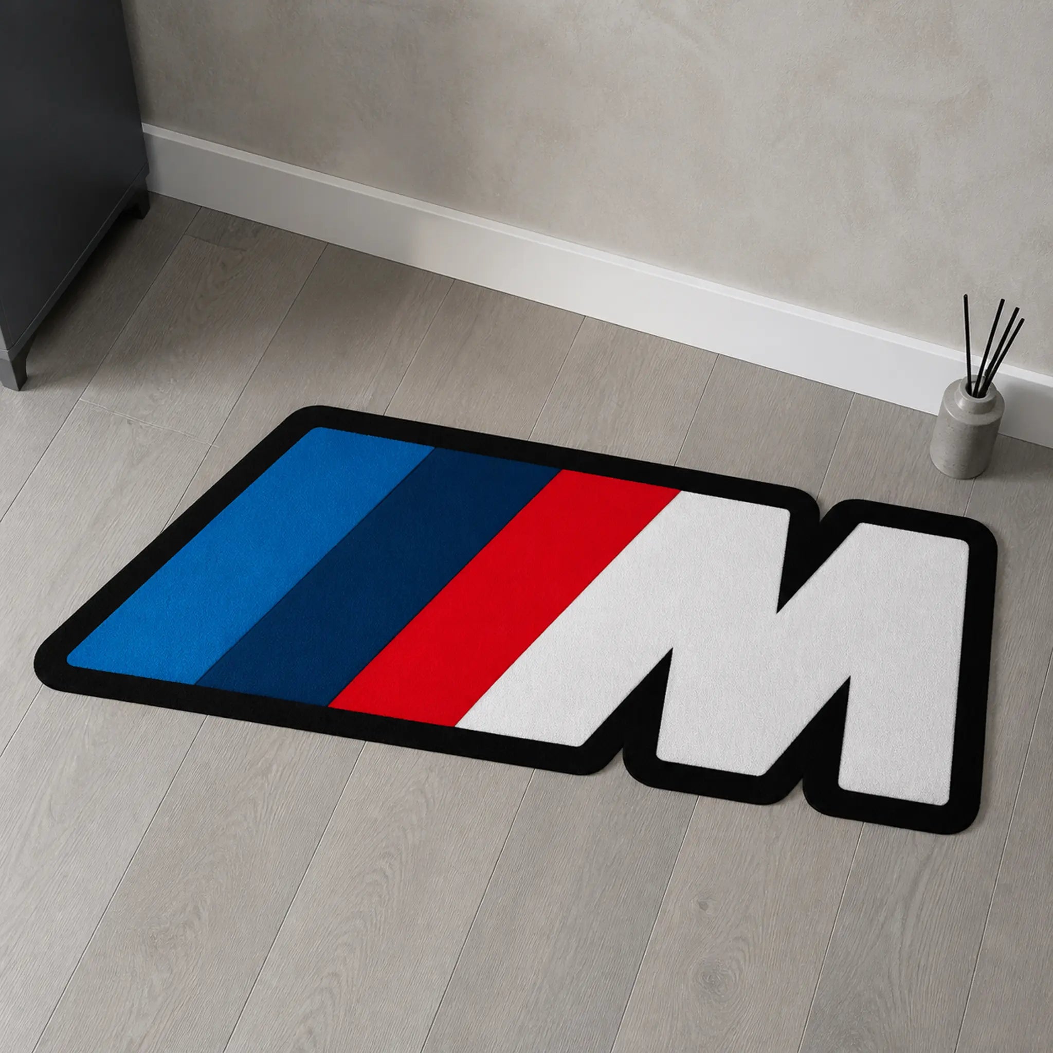 M Performance die-cut rug — BMW M badge with blue, navy and red stripes and a white M, cut to the badge shape with black edge binding