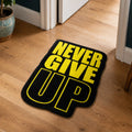 Never Give Up die-cut rug — NEVER GIVE UP in heavy yellow type on black, cut to the shape of the words with black edge binding