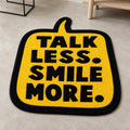SMILE MODE die-cut rug — TALK LESS. SMILE MORE. in black on a yellow speech bubble, cut to the bubble shape with black edge binding