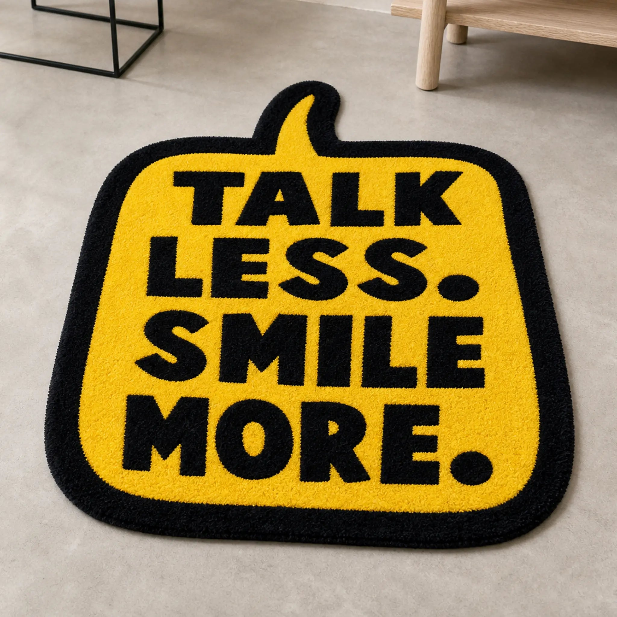 SMILE MODE die-cut rug — TALK LESS. SMILE MORE. in black on a yellow speech bubble, cut to the bubble shape with black edge binding