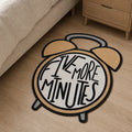 Snooze O’Clock die-cut rug — retro tan twin-bell alarm clock with FIVE MORE MINUTES hand-lettered on the face, cut to the clock shape with black edge binding
