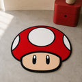 Super Mario power-up mushroom die-cut rug — red cap with white spots and a cream face, cut to the mushroom silhouette with black edge binding