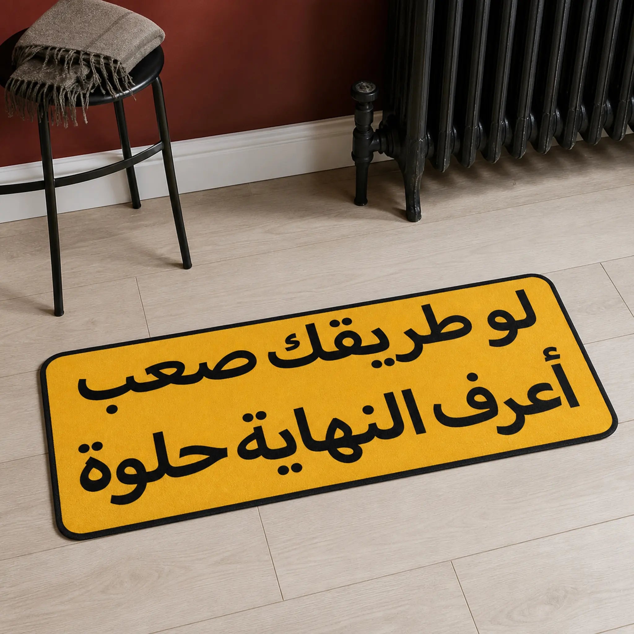 Worth The Road die-cut rug — the Arabic line لو طريقك صعب أعرف النهاية حلوة in black on an amber plaque, cut to the sign shape with black edge binding