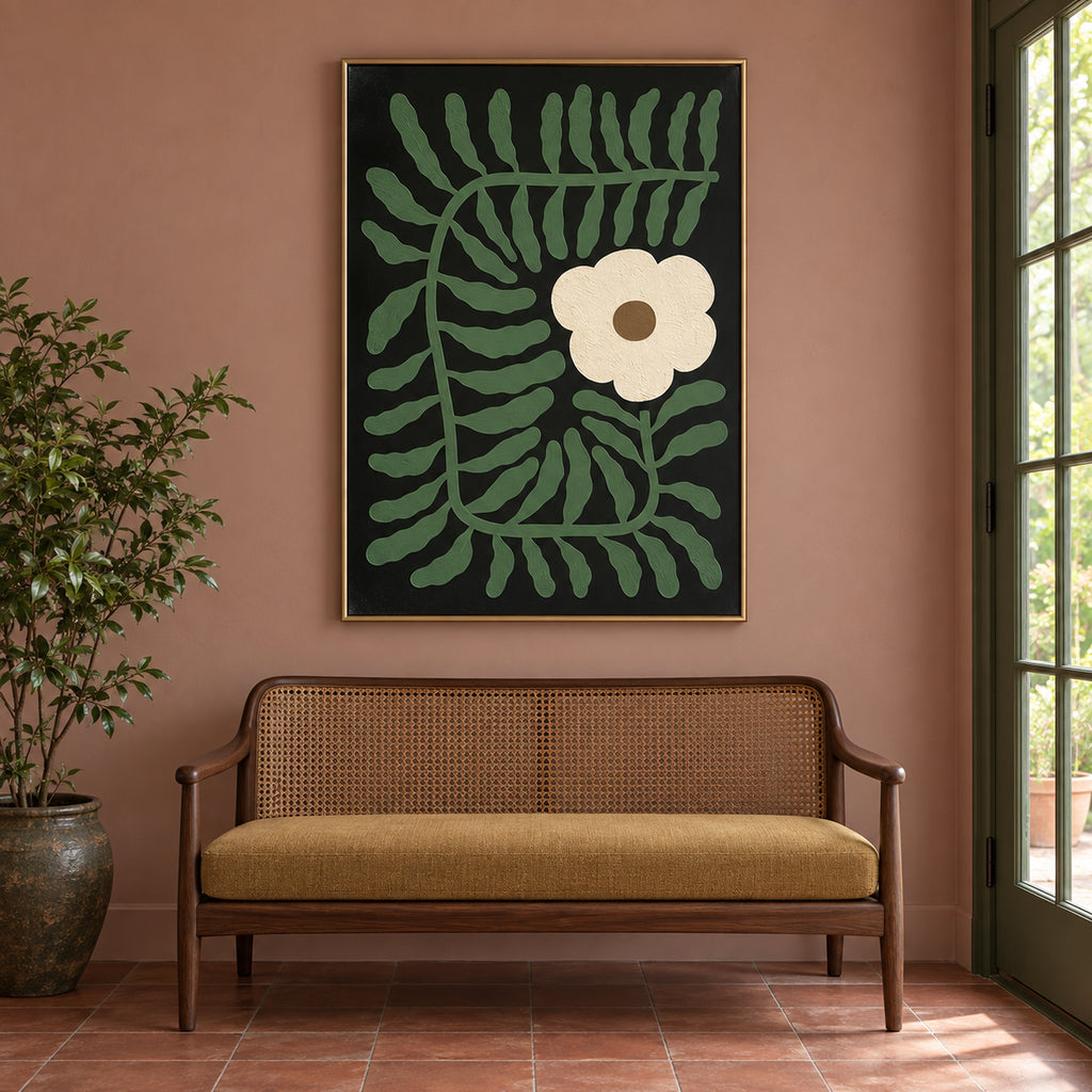 Front view of Fern & Ivory, muted green foliage and an ivory flower on black in a gold frame above a cane-backed bench.