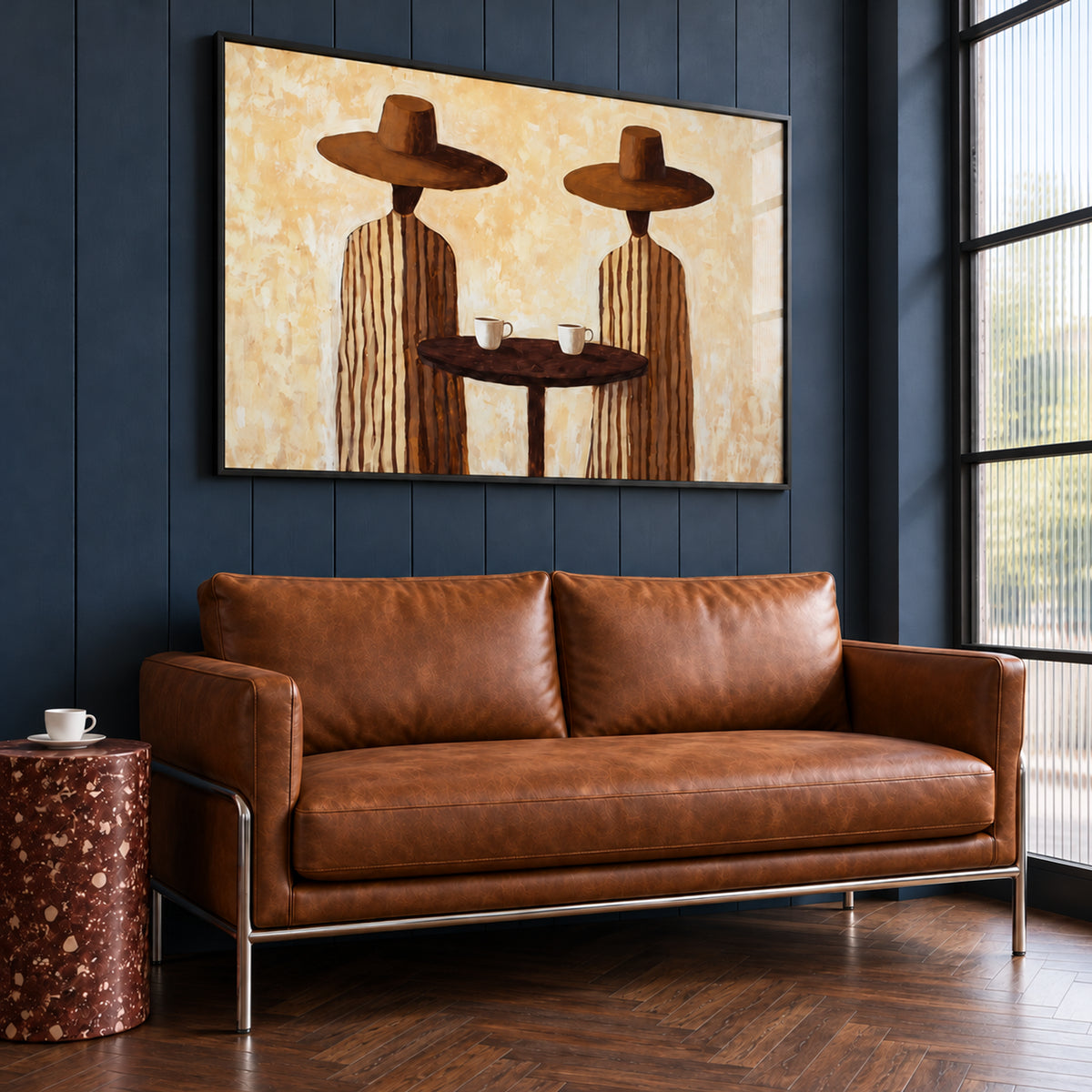 Angled view of Coffee for Two landscape wall art in a slim black frame, displayed above a brown sofa on a dark blue wall.