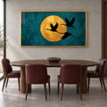 Front view of Gilded Flight gold-framed wall art, showing three black cranes and a golden moon on deep teal above a dining table.