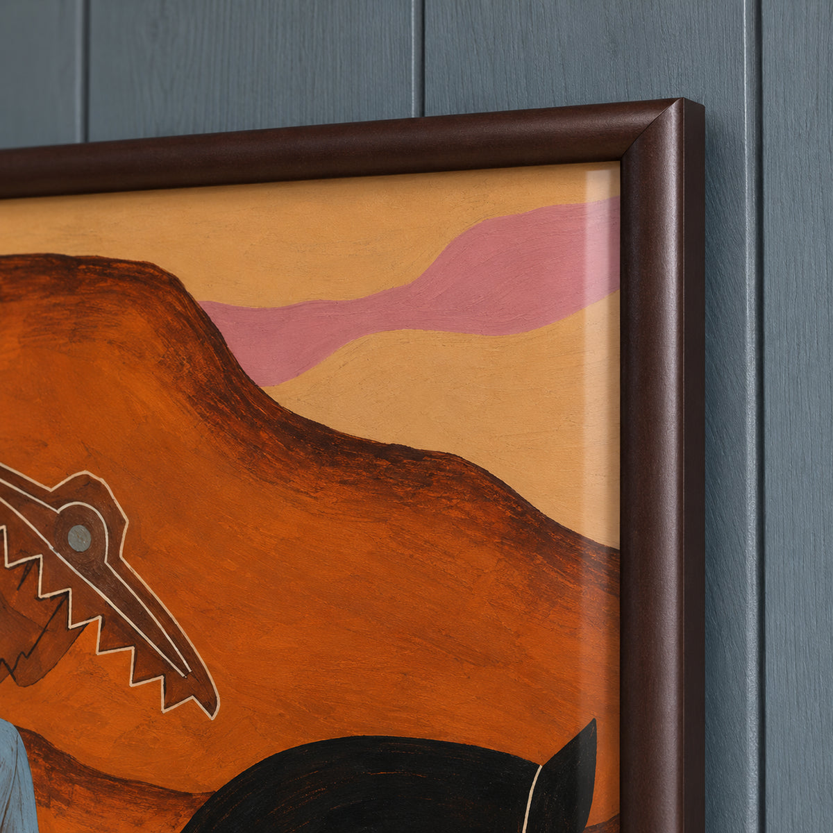 Detail of The Desert Rider's dark brown frame corner beside ochre sky, pink clouds and rust-orange hills.