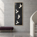 Front view of Quiet Ascent, four ivory doves in flight on a tall charcoal-black background in a gold frame beside a curved staircase.