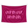 Steady Progress wall tapestry with STEP BY STEP, DAY BY DAY in light pink brush lettering on a deep berry background.