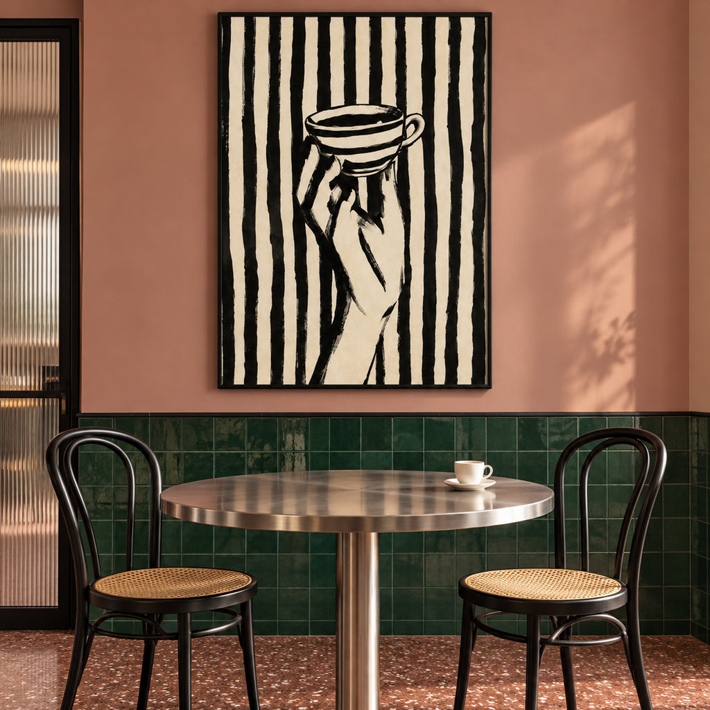 Front view of The Espresso Hour black-framed cup-and-hand artwork above a café table, against pink walls and green tiles.
